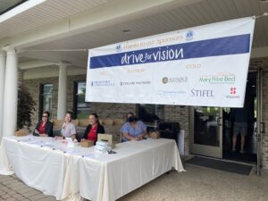 four women by a table under a banner that says "drive for vision"